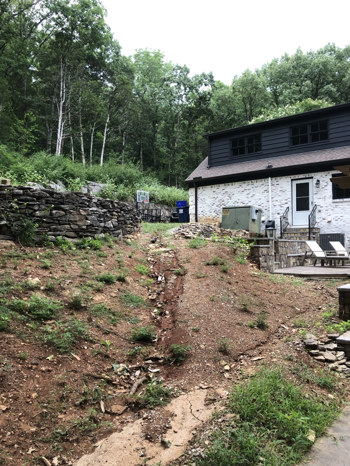 Existing sloped residential site beside the home and stone retaining wall