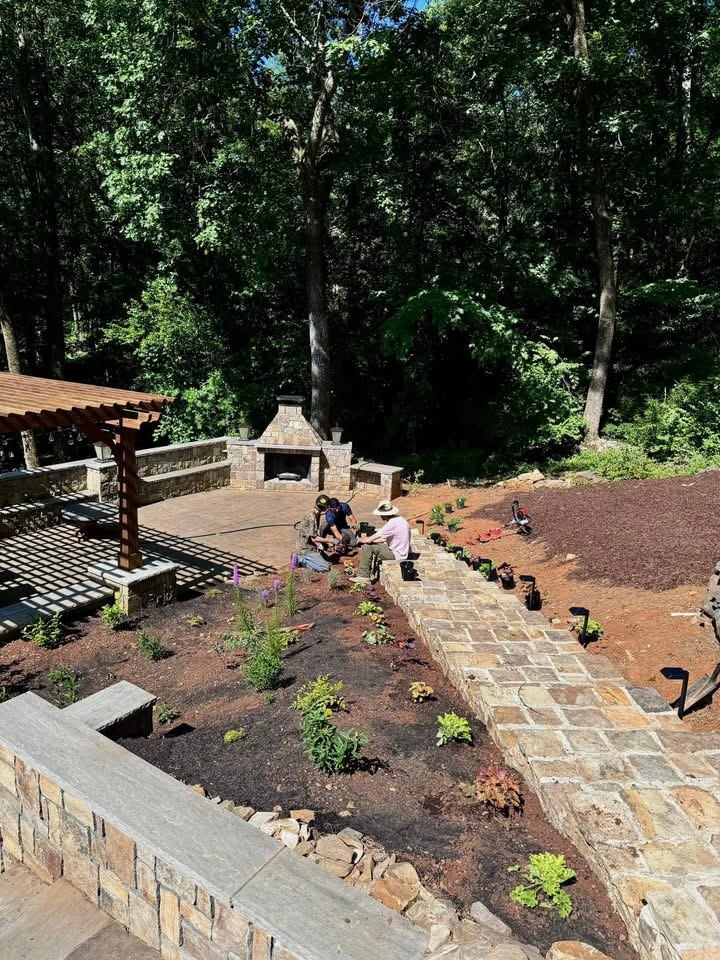 Crew installing plants around the stone path, pergola and outdoor fireplace